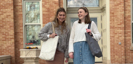 Two girls standing and smiling while carrying temple bags