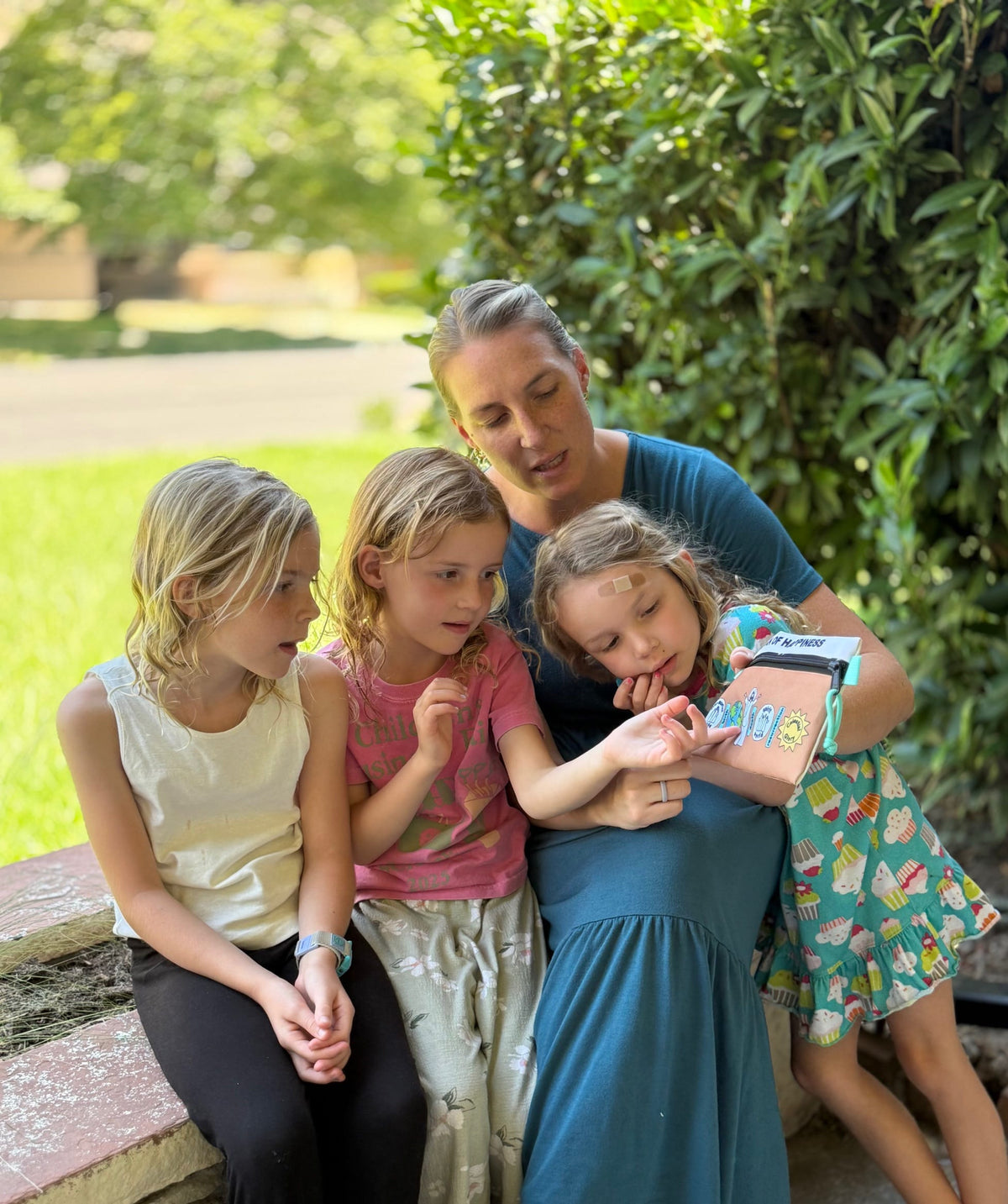 Woman and three girls sitting outdoors, looking at the All In Pouch together.
