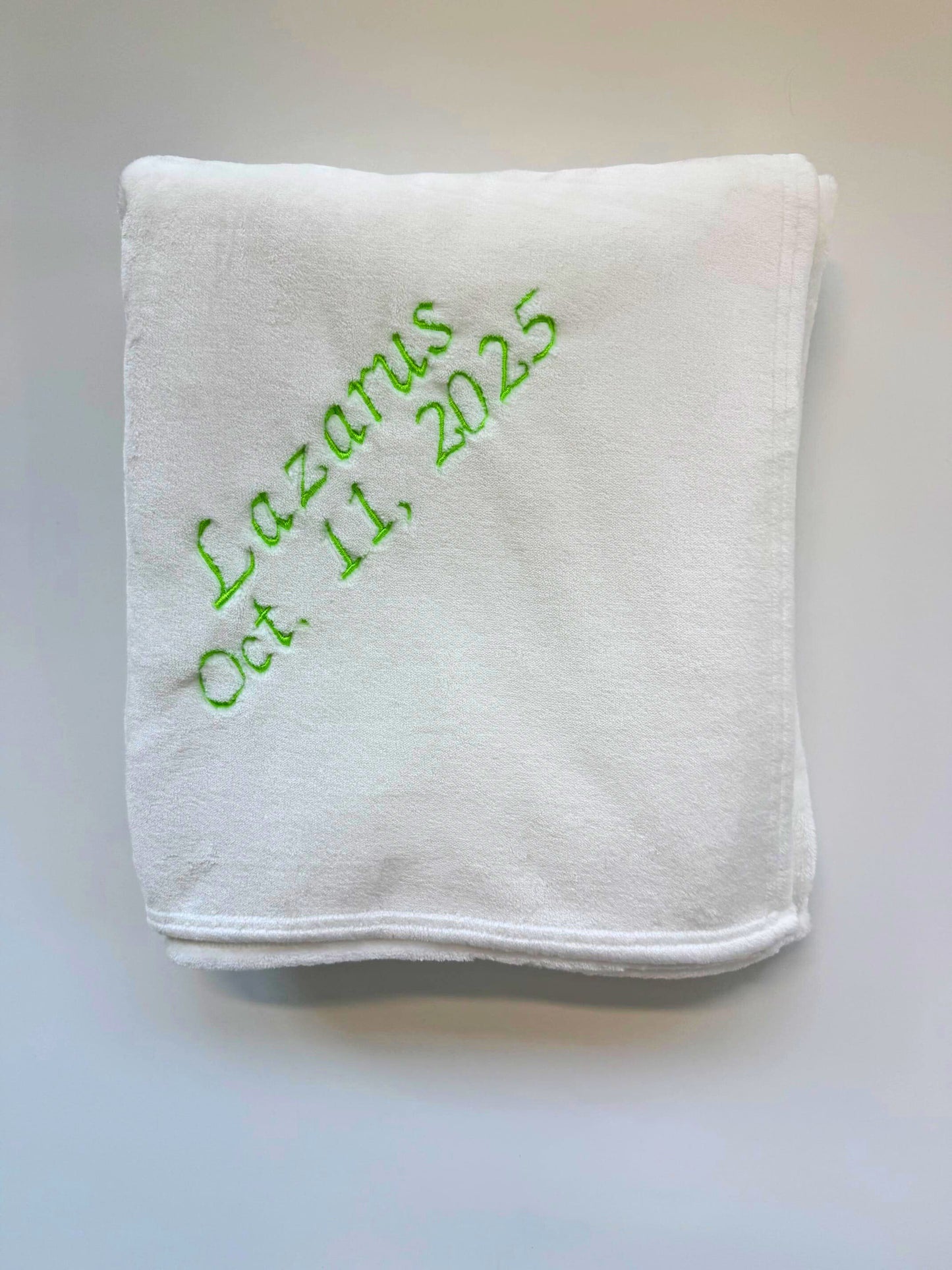 White blanket with green embroidered text on a gray background