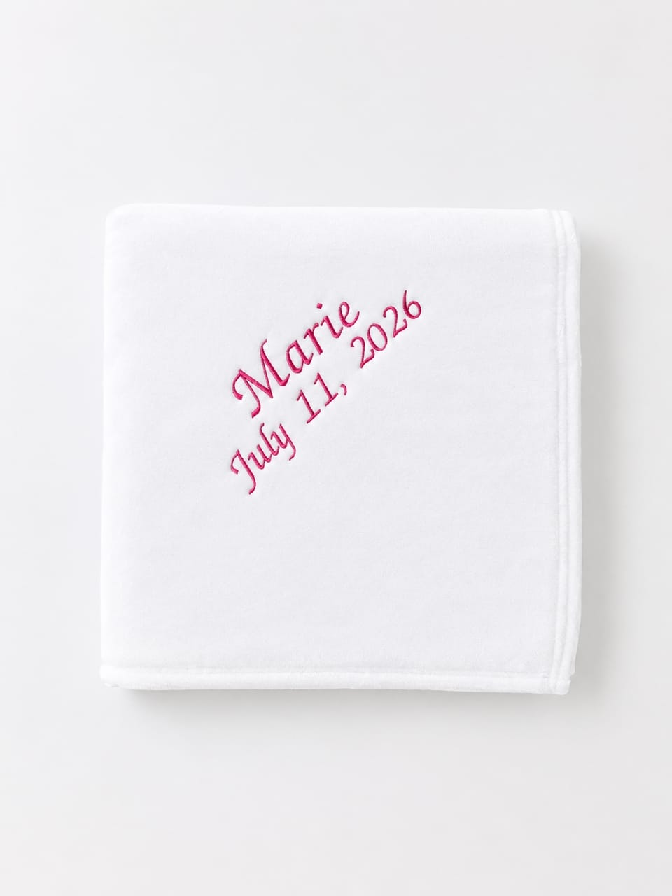 White blanket with the name 'Marie' and the date 'July 11, 2026' embroidered in pink thread