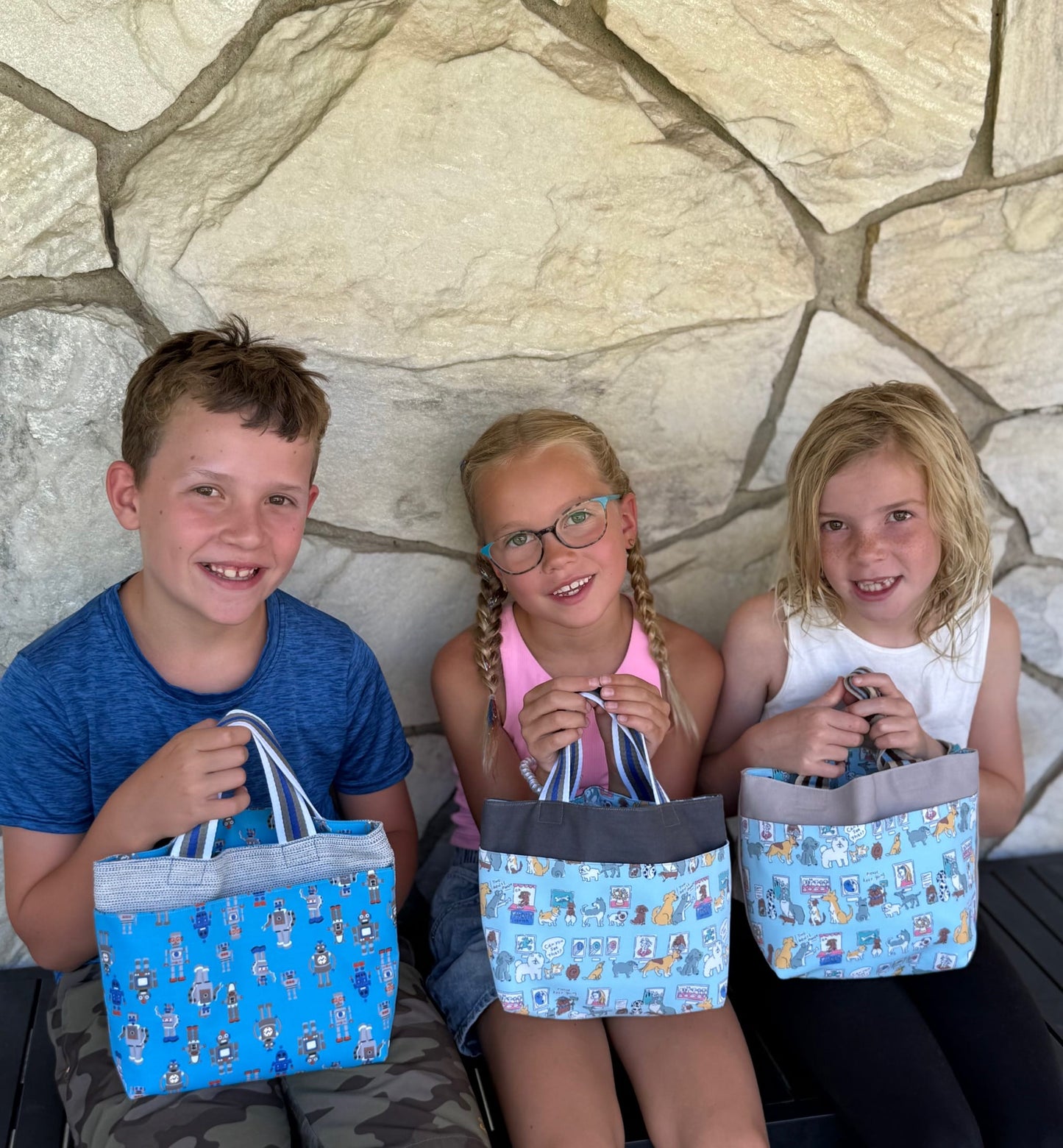 Three children sitting and holding Children's Scripture Bags