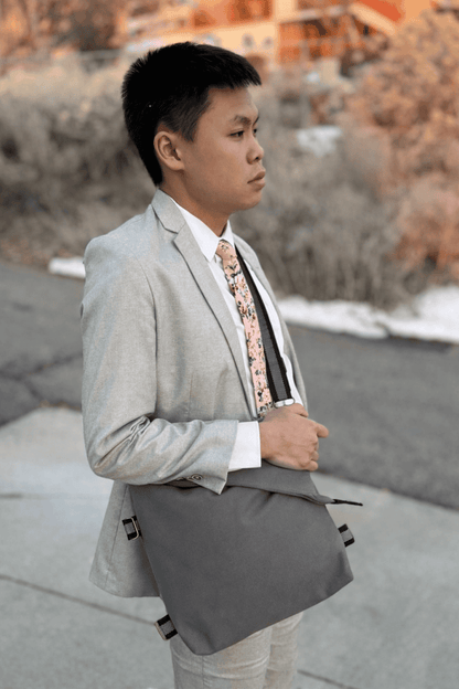 Man in a gray suit with a patterned tie carrying a gray crossbody shoulder bag