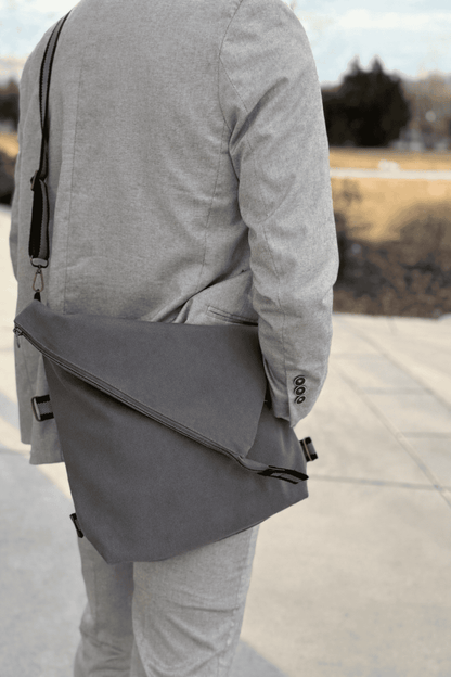 Man wearing a gray jacket and holding a matching gray crossbody shoulder bag outdoors.