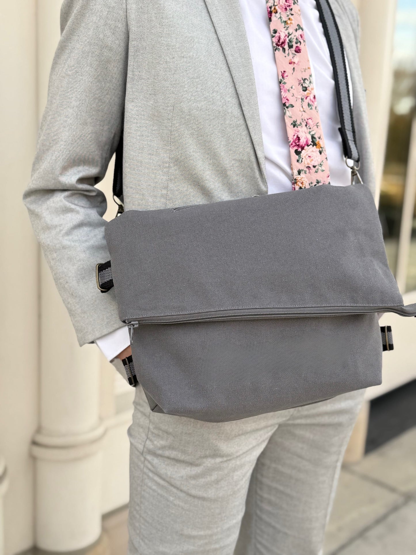 Man wearing a gray suit with a gray messenger bag and floral tie.