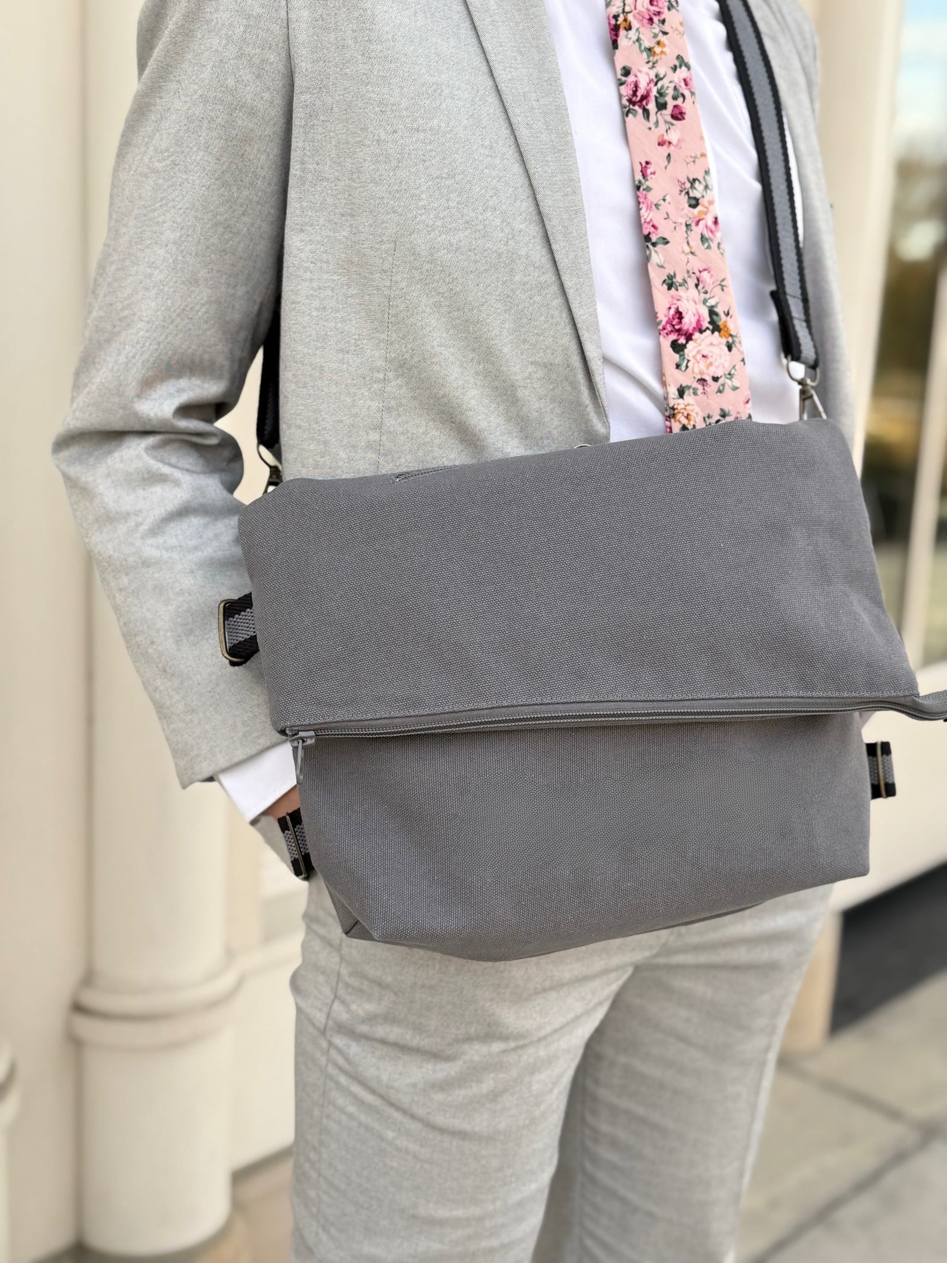 Man wearing a gray suit with a gray messenger bag and floral tie.