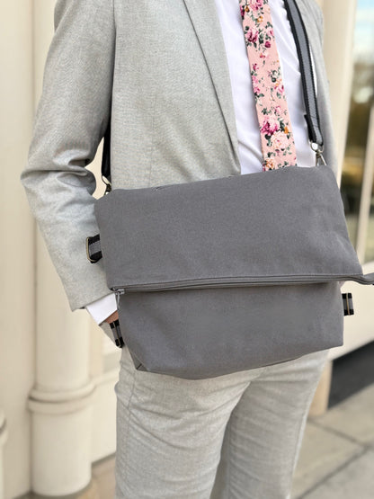 Man wearing a gray suit with a gray messenger bag and floral tie.
