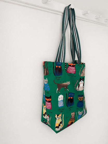 Green tote bag with cat pattern hanging on a white wall