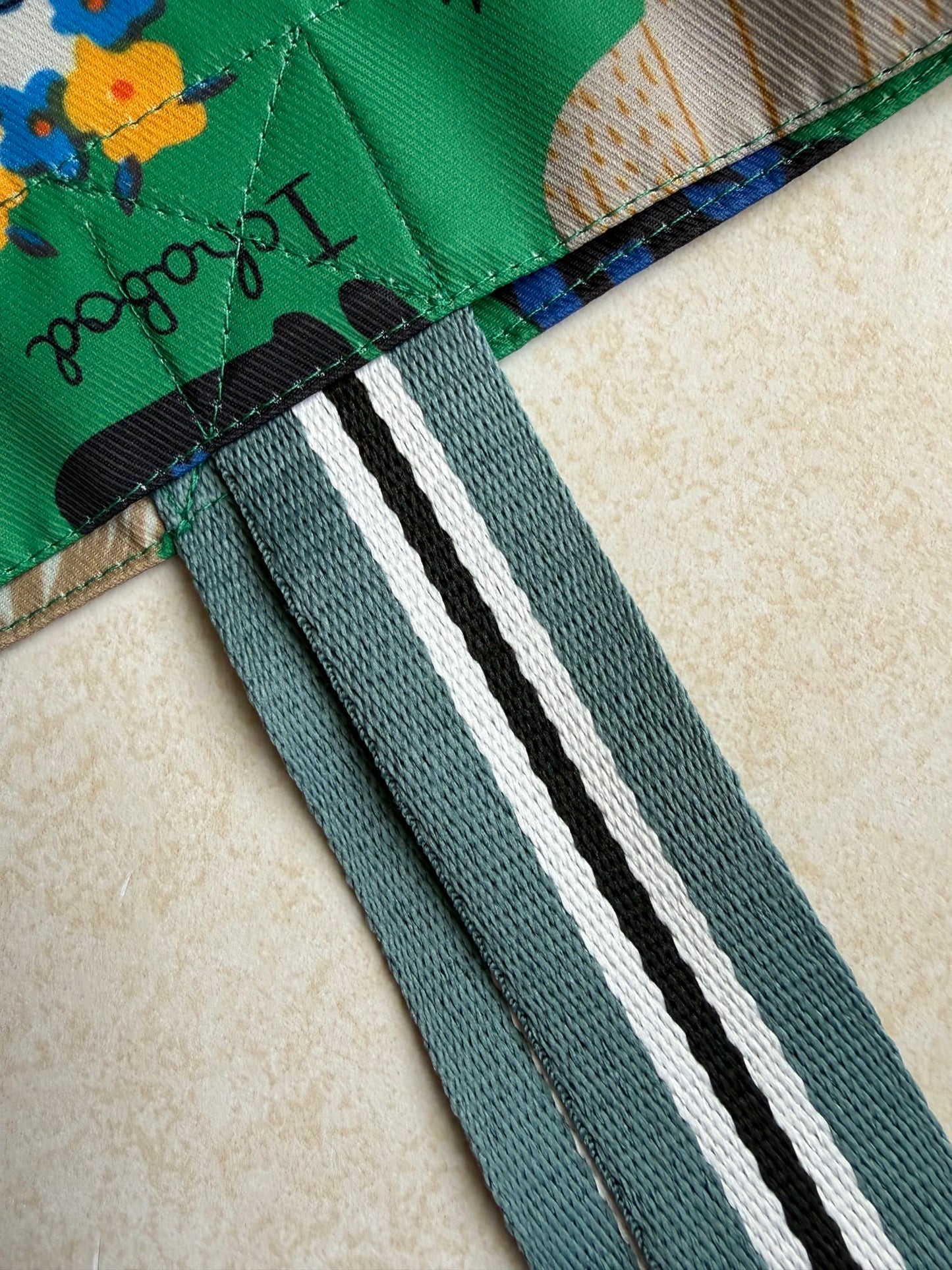 Close-up of a green bag fabric attached to teal colored and black and white striped straps
