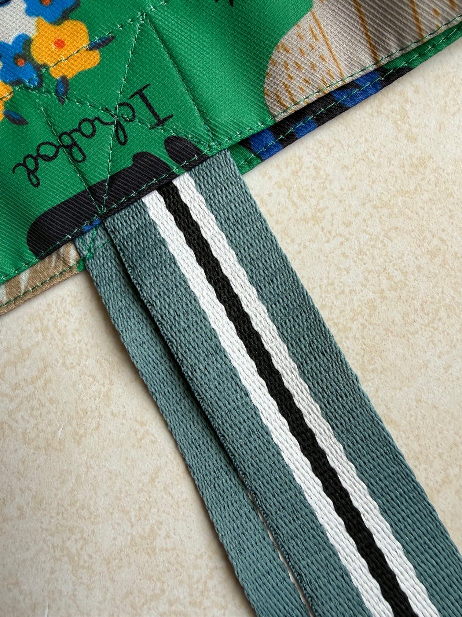Close-up of a green bag fabric attached to teal colored and black and white striped straps