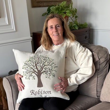 Woman sitting on a couch holding a family tree pillow with the name 'Robison' embroidered.