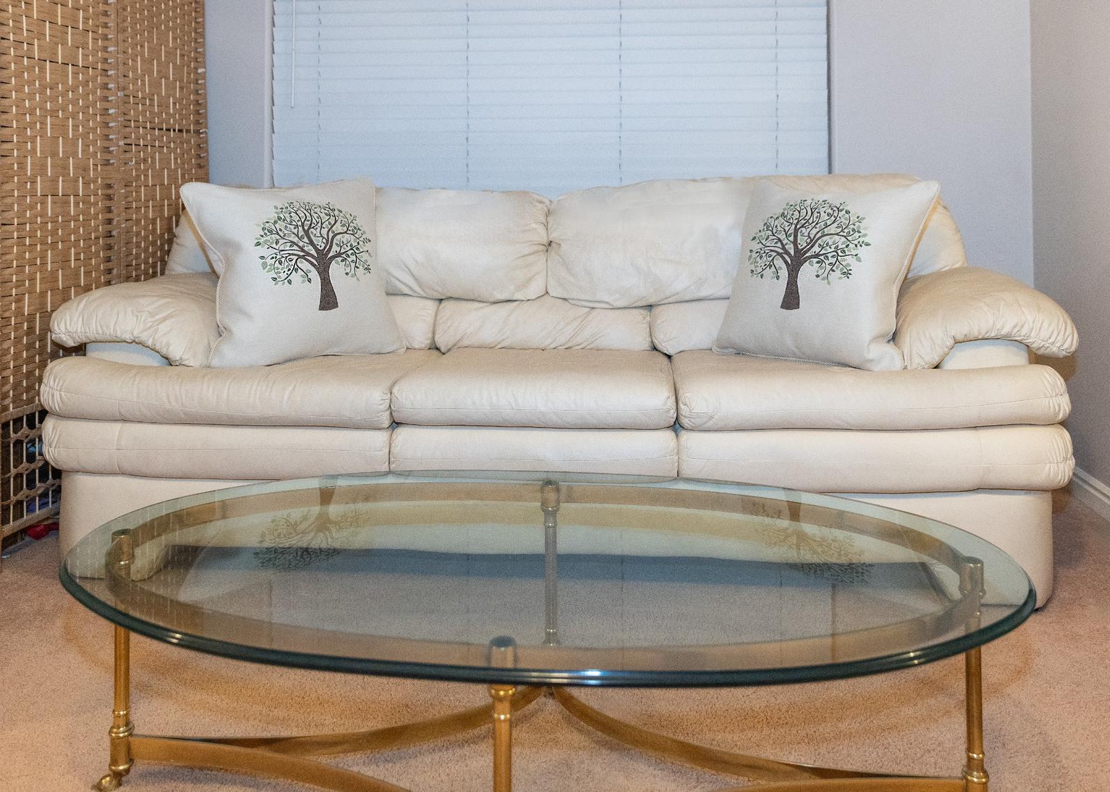 Beige sofa with decorative family tree pillows and a circular glass table in a living room