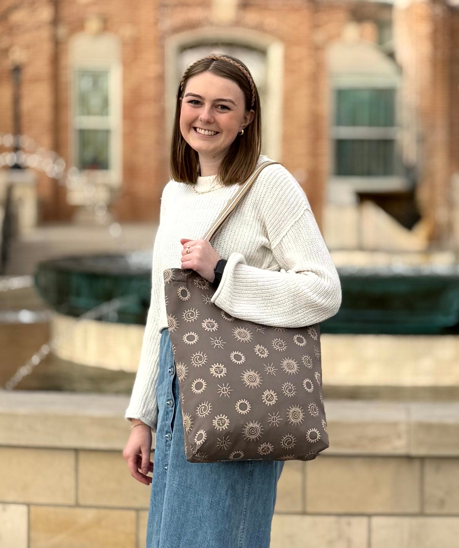 Smiling young woman outside of a temple carrying the sunstones print LDS tote bag over her shoulder