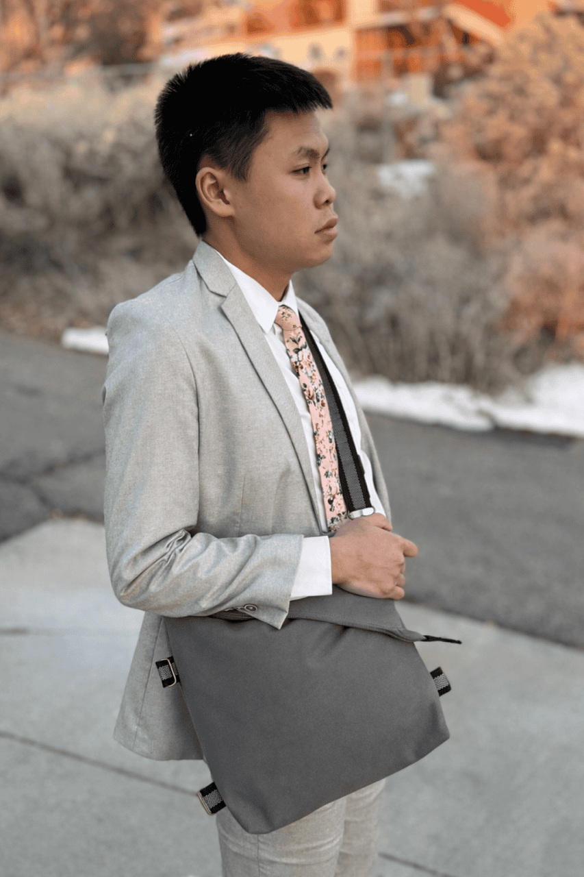 Man in a gray suit with a patterned tie carrying a gray crossbody shoulder bag