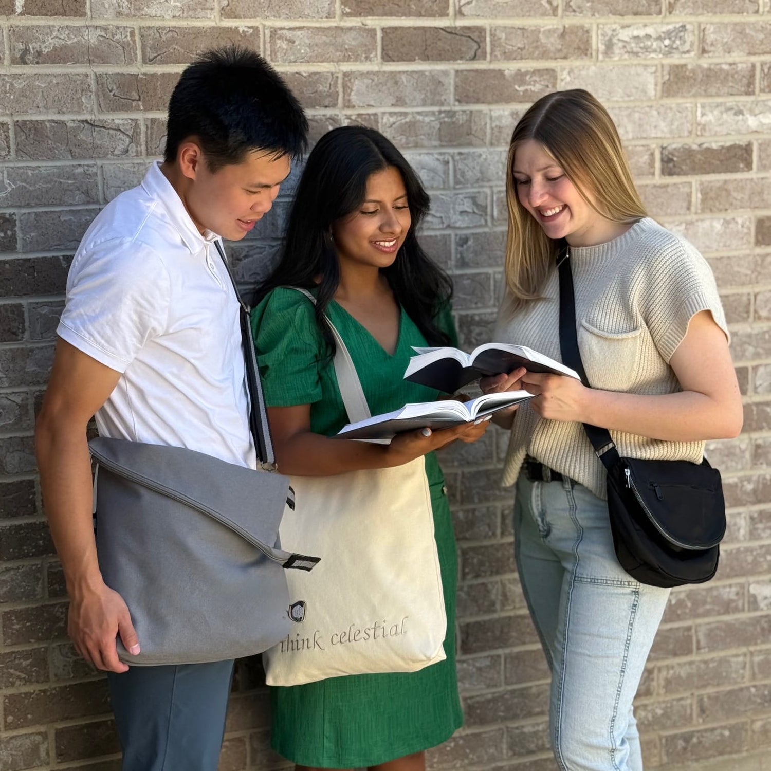Three individuals standing and carrying bags, looking at books.