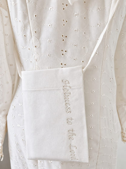 White cotton temple pouch embroidered with the phrase “Holiness to the Lord,” worn in front of a white eyelet temple dress.
