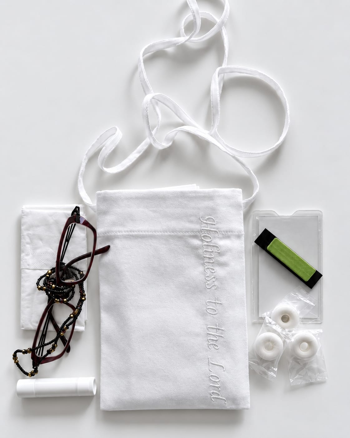 White cotton pouch with a lanyard displayed next to tissues, eyeglasses, lip balm, card holder, name badge, and breath mints
