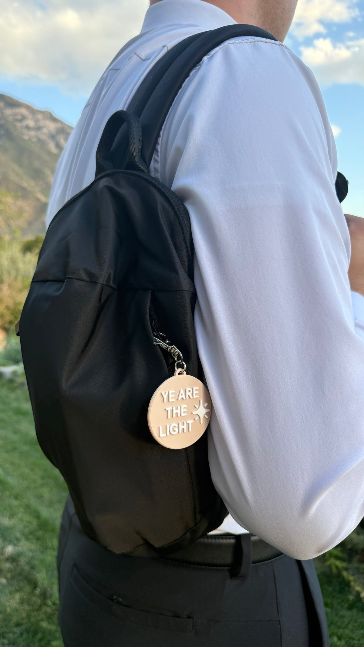 Black LDS Mission Ready Convertible Bag worn over one shoulder against the back, with a “Ye Are the Light” charm