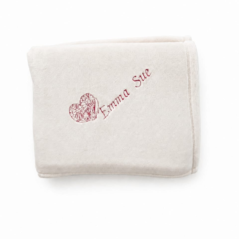 Folded white blanket with an embroidered heart design and the name 'Emma Sue'