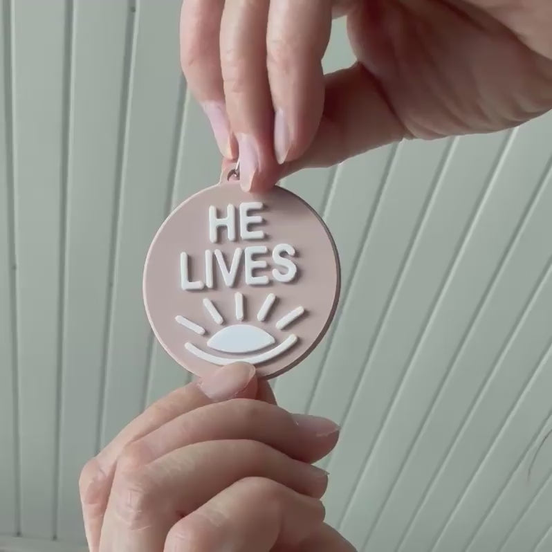 Demonstration of the two sides of the bag charm. One side with the words "He Lives and the other "Ye Are the Light"