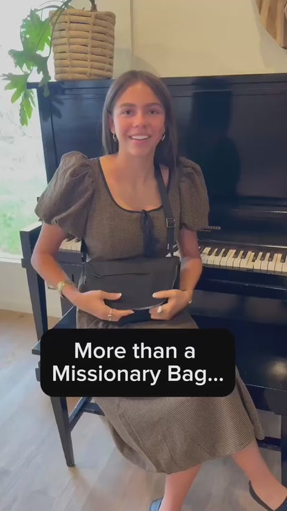 A young woman opens a black crossbody missionary bag to show its interior compartments and colorful scripture-patterned lining