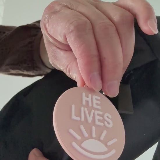 Demonstration of the two sides of the bag charm. One side with the words "He Lives and the other "Ye Are the Light"